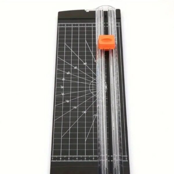 A paper trimmer featuring a measurement grid and a sliding blade with an orange handle.